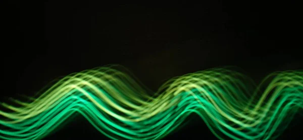 Neon green light wave pattern abstract streaming through the isolated black background with copy space for inscription and adding . Made with long exposure technique , light painting