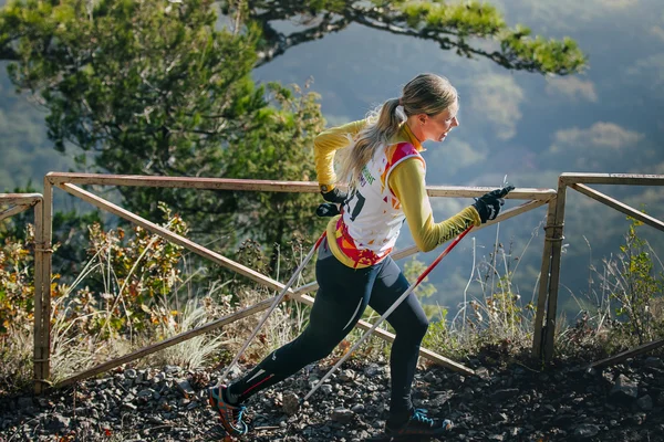 young woman athlete running on mountain trail with nordic walking poles