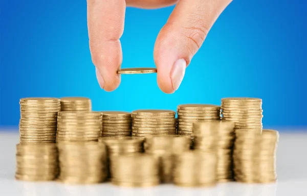 Nahaufnahme Hand legt Münze auf Stapel Münzen vor blauem Hintergrund — Stockbild Hand Münze auf Münzen — Stockfoto