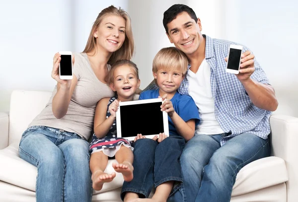 Familia sentada en el sofá con aparatos electrónicos —  Fotos de Stock