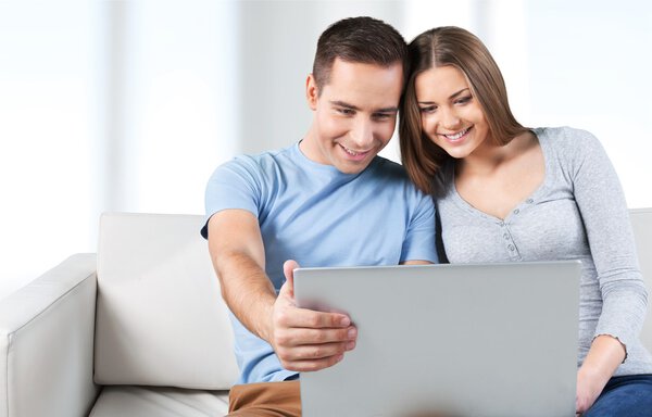 улыбающаяся пара с ноутбуком на диване
