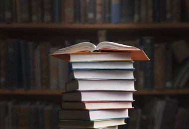 A stack of new study books on the table against the background of a bookshelf in library.
