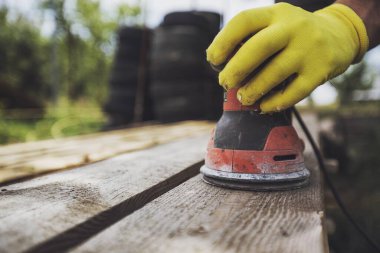 Carpenter at workshop polishes wooden board on natural background