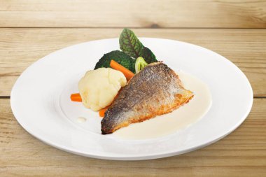 Kızarmış balık filetosu ve ahşap masada servis edilen sebze salatası.