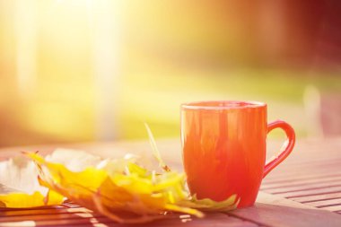 Sonbahar yaprakları ve sıcak bir fincan kahve. Altın gün batımına karşı ahşap masa ya da gündoğumu ışığı arka planı. Sonbahar, boş zaman ve kahve molası konsepti.