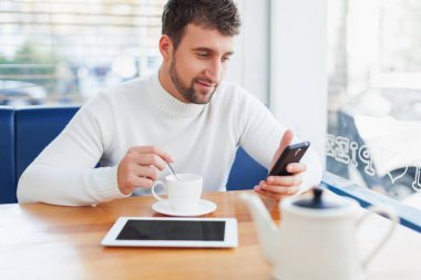 Kafede cep telefonu kullanan genç bir adam.