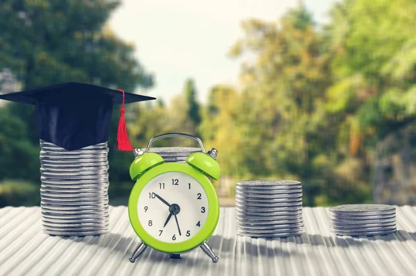 Public school funding / education funding, financial concept : Black graduation cap / hat, family members and kid, US dollar bag on rows of rising coins, white clock on a table, green bokeh background
