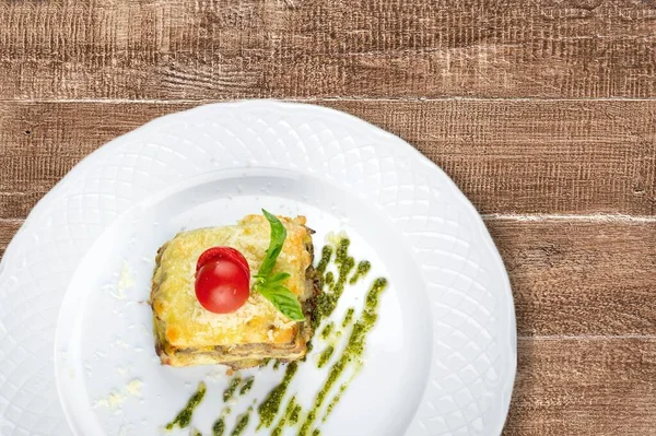 Beyaz bir tabakta fesleğen yaprağıyla servis edilen lezzetli bir lazanya. Ben...