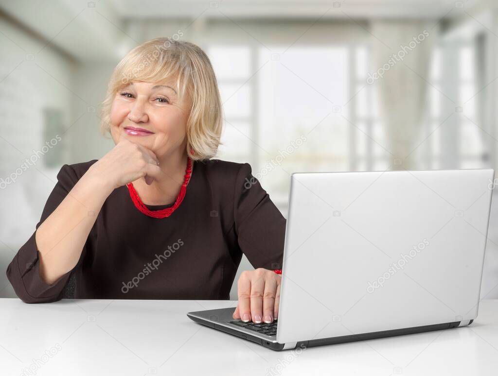 Smiling stylish mature woman sits at a desk with laptop