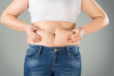 Kot pantolonlu ve gömlekli bir kadın göbeğini sıkıyor. Diyet ve yağ kaybı kavramı.