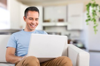 Düşünceli genç bir adam evinde bir masada oturup bir dizüstü bilgisayarla çalışıyor..