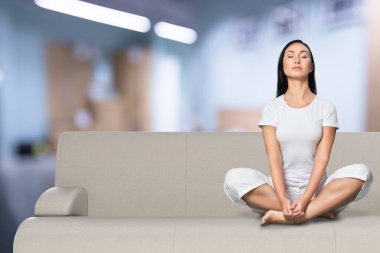 Yoga egzersizleri yapan, bacak bacak bacak üstüne atmış, kanepede oturan konsantre genç bir kadın..