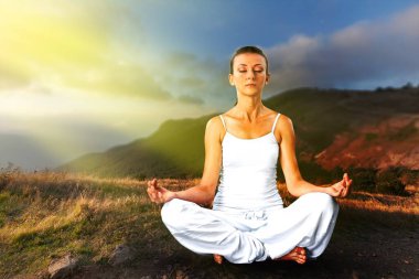 Genç bir kadın dağın tepesinde yoga yapıyor.