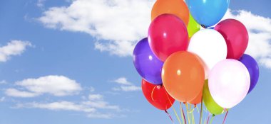 Mavi gökyüzünde helyumlu ve bulutlu bir grup renkli balon.