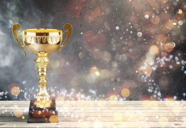 Ahşap masanın üzerinde güzel altın bir kupa ve soyut parlak ışıklarla karanlık bir zemin.