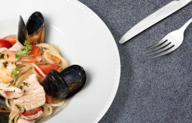 Beyaz tabakta deniz ürünleri ve sebzeli spagetti.