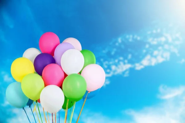 A bunch of multicolored balloons with helium on a blue sky and clouds background