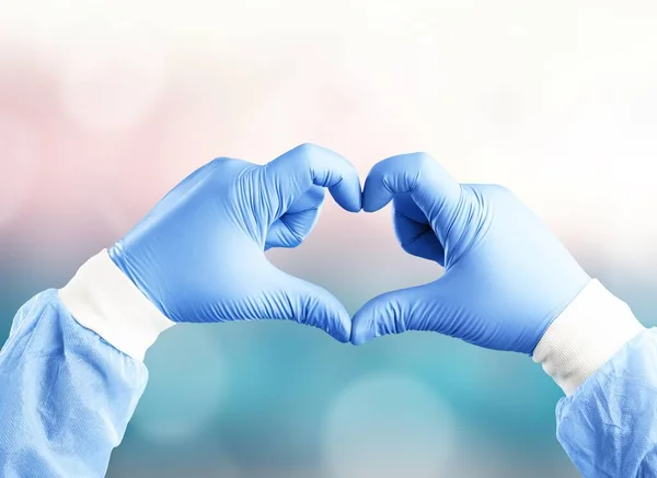 Doctor or nurse in protective gloves shows the symbol of the heart. Love, care and safety symbol.