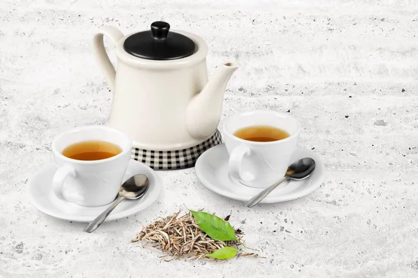 Herbal tea with white tea cups and teapot, with green tea leaves.