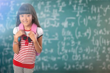 Parmağını kaldırmış gözlüklü, gülümseyen mutlu çocuk ilk kez okula gidiyor. Okul çantası ve kitabı olan bir çocuk. Sınıfın arka planında tahtası olan bir çocuk. Okula geri dön..