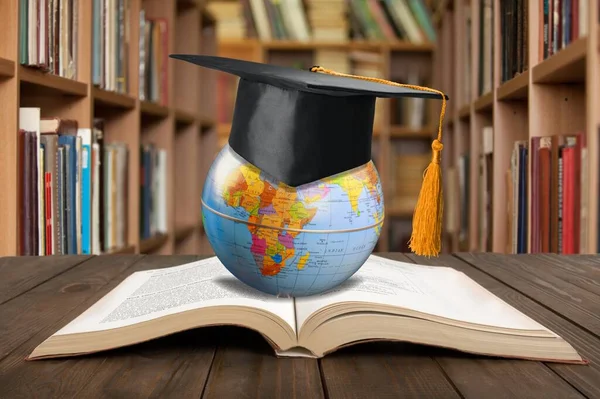 Graduated hat, open book and world globe on desk