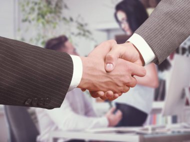 Bilinmeyen iş adamları modern ofis arka planında sözleşme imzaladıktan sonra el sıkışıyor.