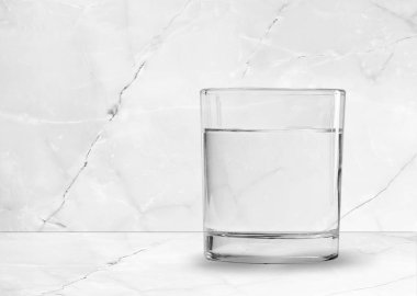 Bir bardak temiz su beyaz masanın üzerinde güneş ışığı ve camın gölgesi.