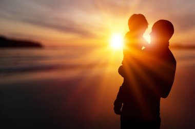 Ebeveynlerin elindeki çocuk gülüyor. Mutlu aile gün batımında sahilde yürüyor..