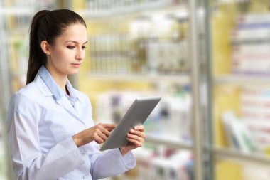 Genç eczacının elleri, tıbbi malzeme deposunda dijital tablet kullanarak envanteri kontrol ediyor.