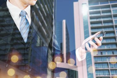 Siyah takımlı genç adam bulanık Megapolis şehrinin arka planında telefona bakıyor..