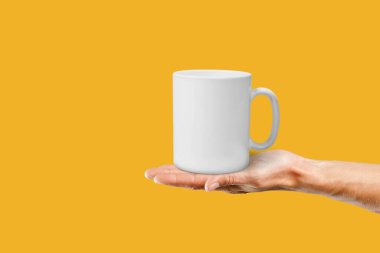 Boş seramik beyaz kahve fincanı ya da sarı arka plandaki kadın ellerinde kupa..