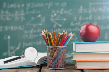 Tahta duvarda kitap, kalem ve elma olan bir çalışma masası.