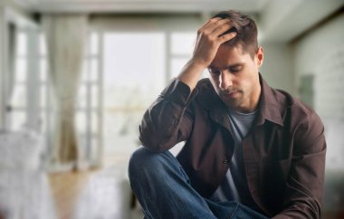 Evde başı ağrıyan üzgün bir adam, kafasına dokunuyor..