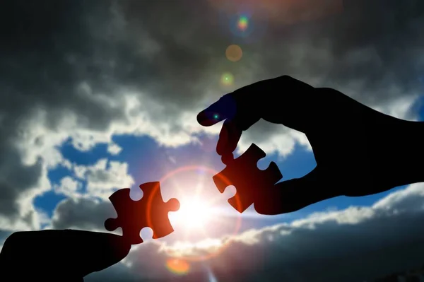 Puzzle pieces connecting with hands on sunset sky background