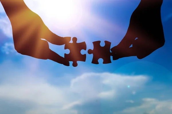 Puzzle pieces connecting with hands on sunset sky background