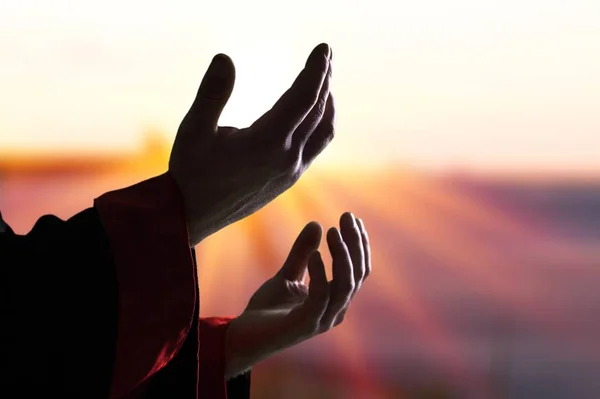 Jesus Christ reaching out his hands and praying at sunset background