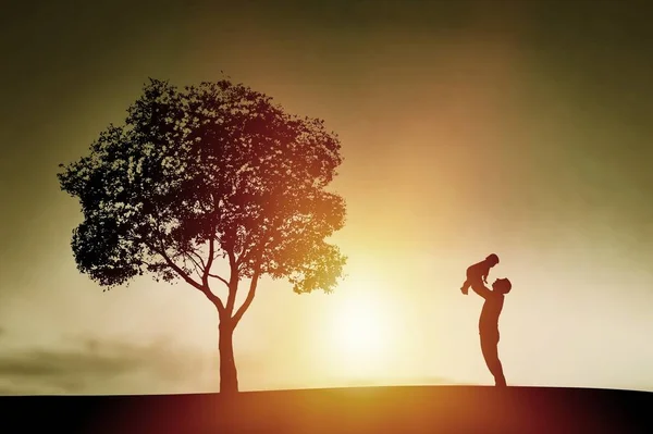 幸せな親は草原で日没の光線の下で腕の中で赤ん坊と遊ぶ — ストック写真
