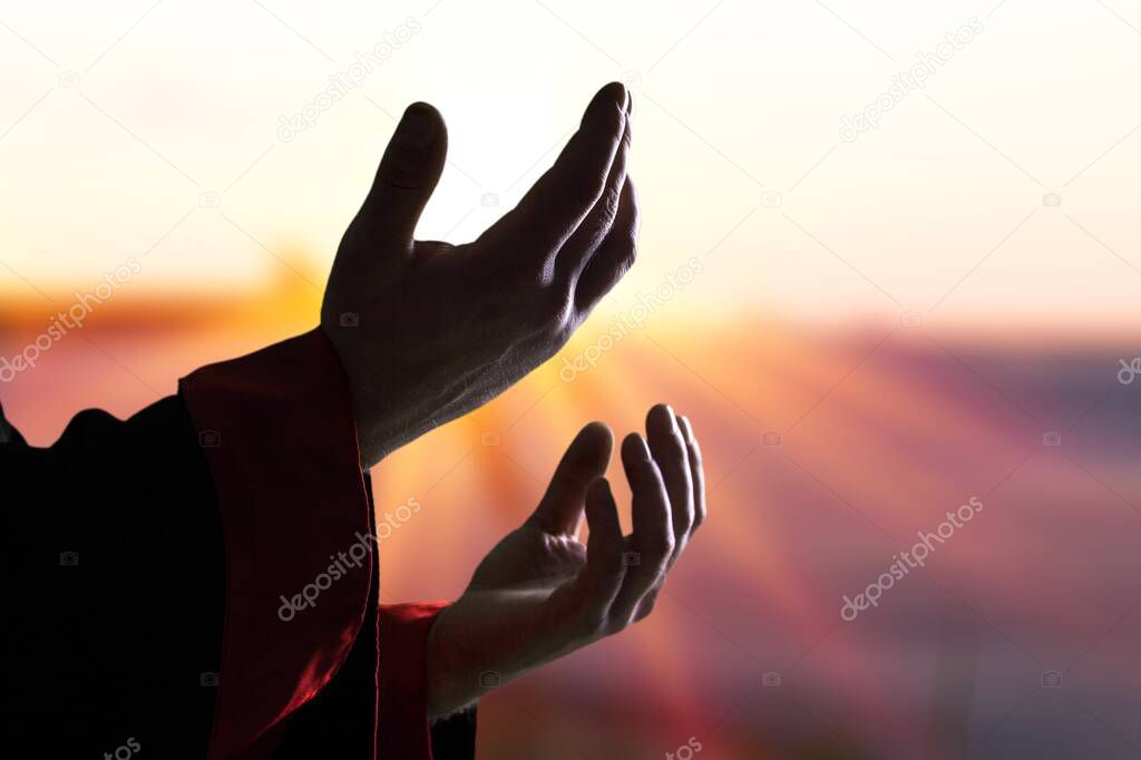 Jesus Christ reaching out his hands and praying at sunset background