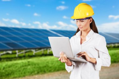 Güneş panelleri alanında özel üniformayla duran güzel bir iş kadını. Kadın mühendis dışarıda çalışmak için dizüstü bilgisayar kullanıyor..