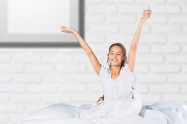 Sakin, genç, eğlenceli, pozitif kadın pijama giyiyor, yatakta yatıyor.