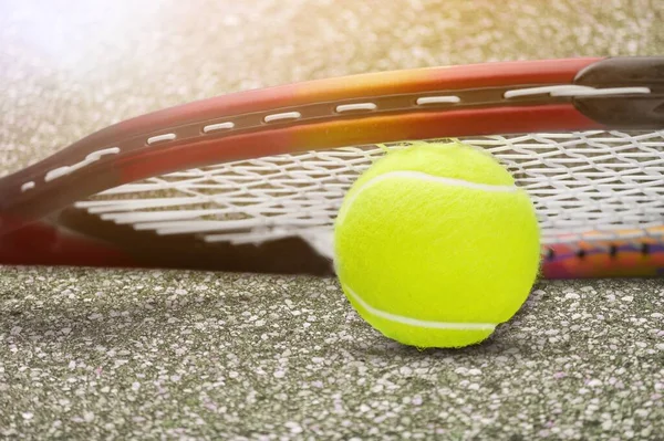 Tenis racket and yellow ball on a green court in the sunset