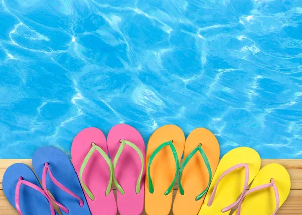 Colored flip flops sitting on the edge of a swimming pool.