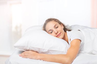 Pijamalı genç bir kadın yumuşak bir yatakta uyuyor.