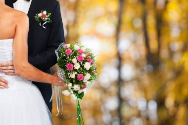 Gelin ve damat birbirlerine sarılıp düğün buketini tutuyorlar.