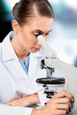 Tıbbi mikroskop kullanarak test sonuçlarını analiz eden bilim kadını.