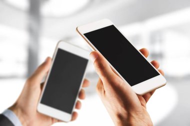 İnsan ellerinde boş ekranları olan iki modern akıllı telefon.
