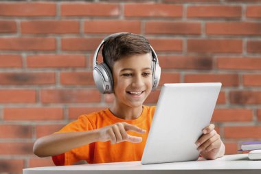 Bilgisayarlı ve kulaklıklı çocuk evde ödev yapıyor.