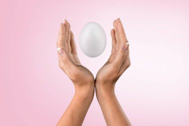 Arka planda beyaz bir yumurta tutan el.