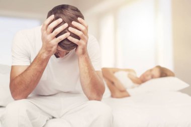 Yatakta oturan depresyonlu genç adam uykusuzluktan uyuyamaz.