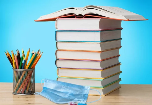 stack of books and pencils with face mask on  background.